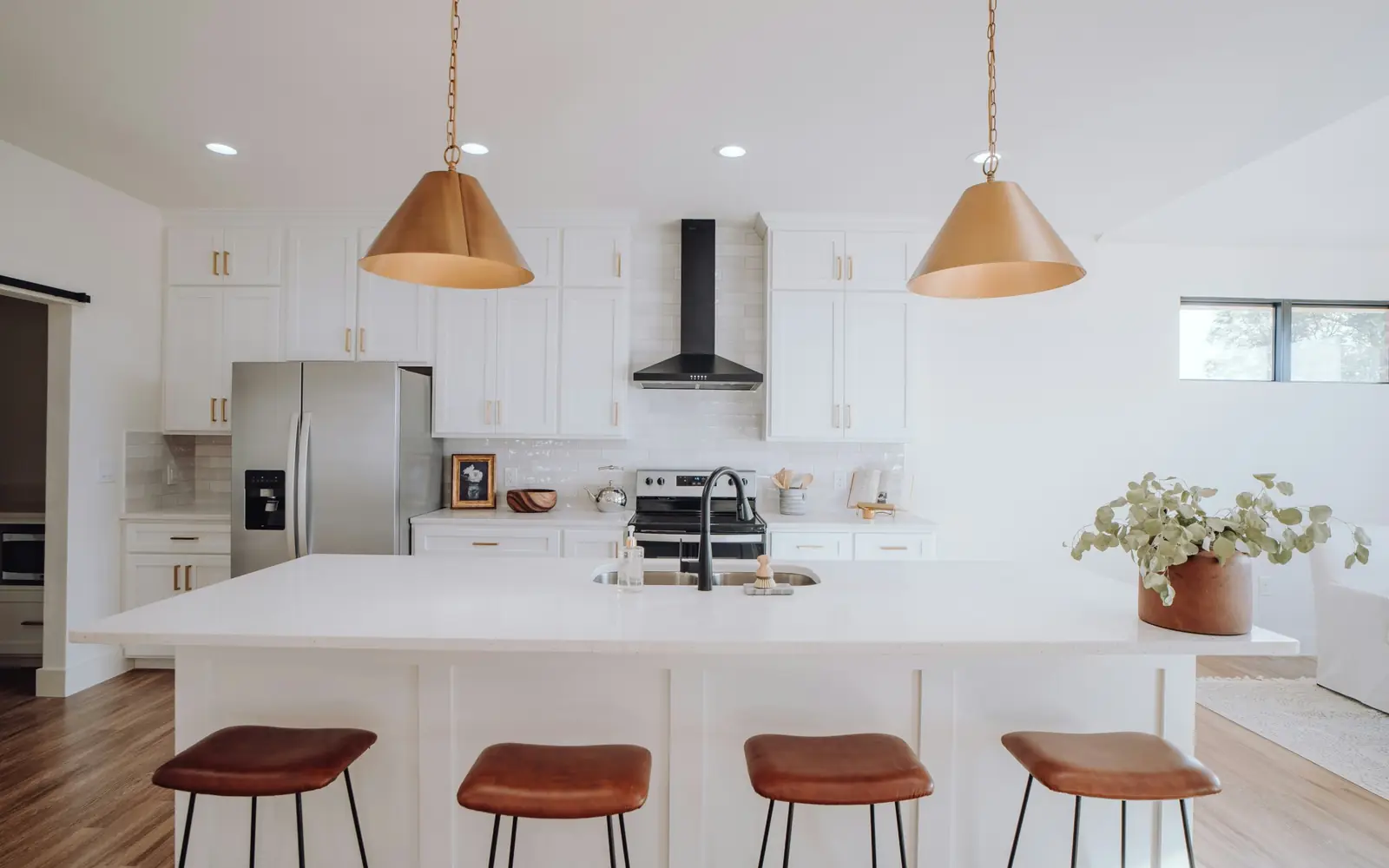 White kitchen with shaker cabinets, a large quartz island, leather stools and brass cone pendants