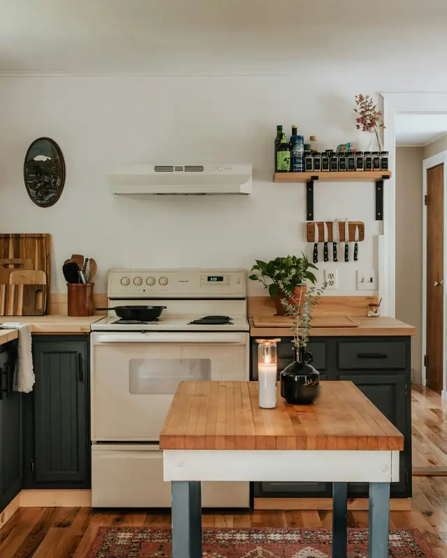 Kitchen with dark painted cabinets, butcher block counters and a wood-top island on a red rug