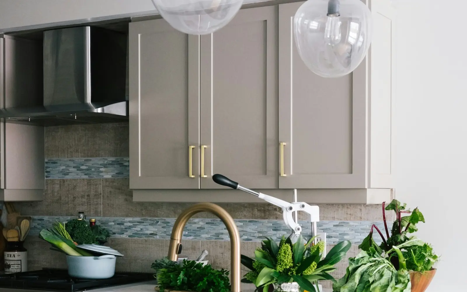 Greige painted shaker cabinets with brass pulls above a white quartz countertop and brass faucet