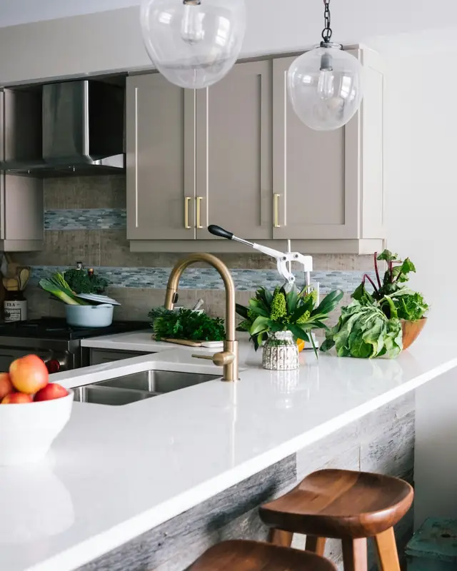 Greige painted shaker cabinets with brass pulls above a white quartz countertop and brass faucet