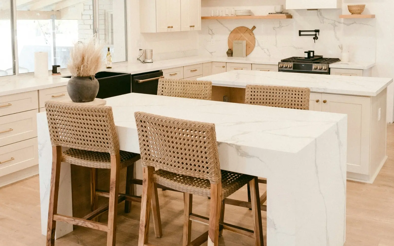 Bright kitchen with a white marble-look waterfall island, woven counter stools and white shaker cabinets