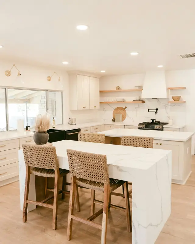 Bright kitchen with a white marble-look waterfall island, woven counter stools and white shaker cabinets