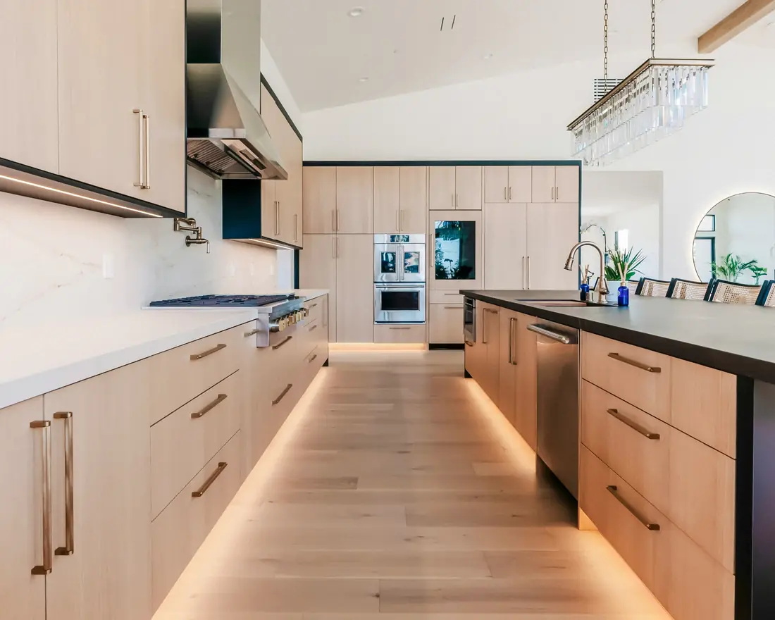 Long kitchen with white oak cabinets, white stone countertops, a dark island top and under-cabinet lighting