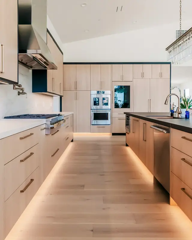 Long kitchen with white oak cabinets, white stone countertops, a dark island top and under-cabinet lighting