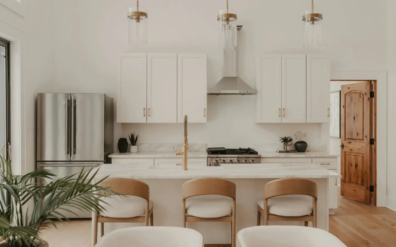 White kitchen with shaker cabinets, a marble-look island, brass faucet and wood counter stools