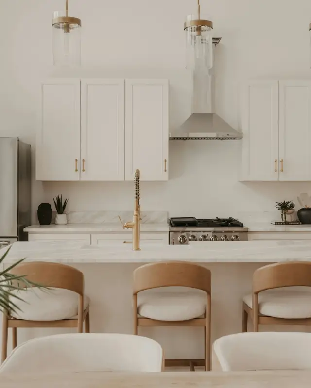 White kitchen with shaker cabinets, a marble-look island, brass faucet and wood counter stools