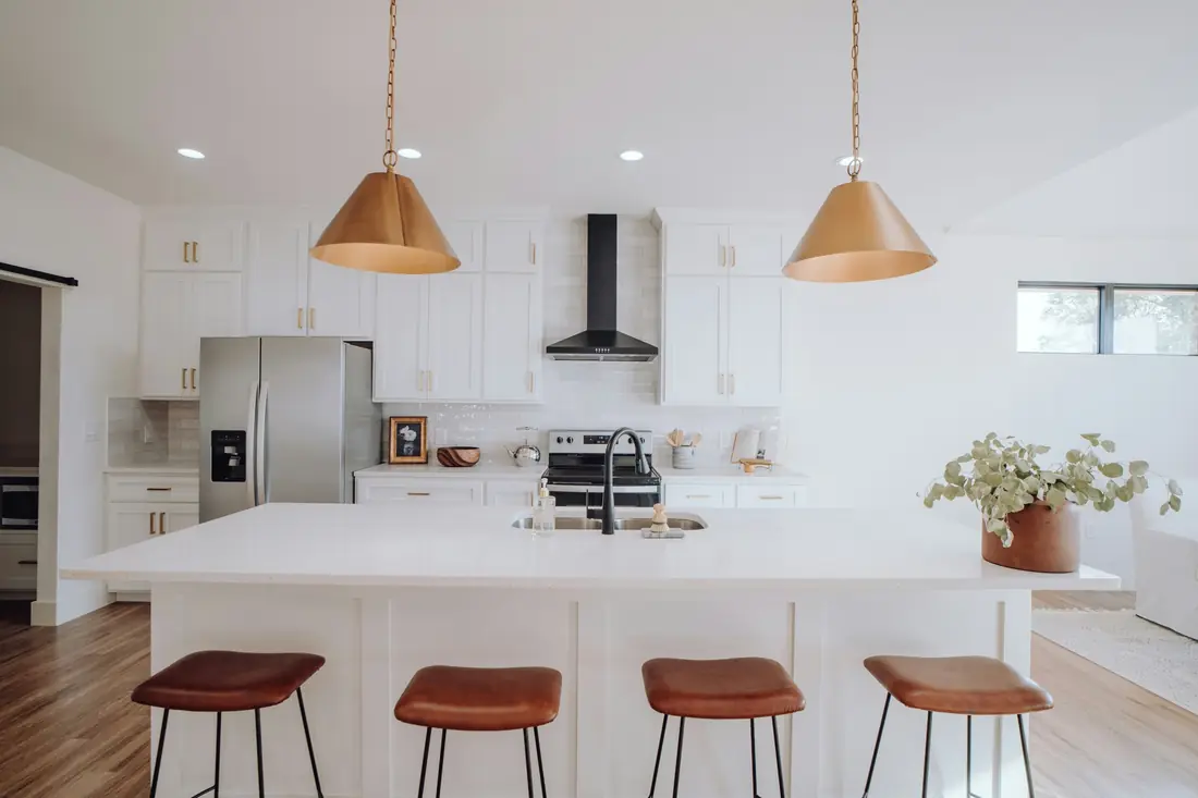 White kitchen with shaker cabinets, a large quartz island, leather stools and brass cone pendants