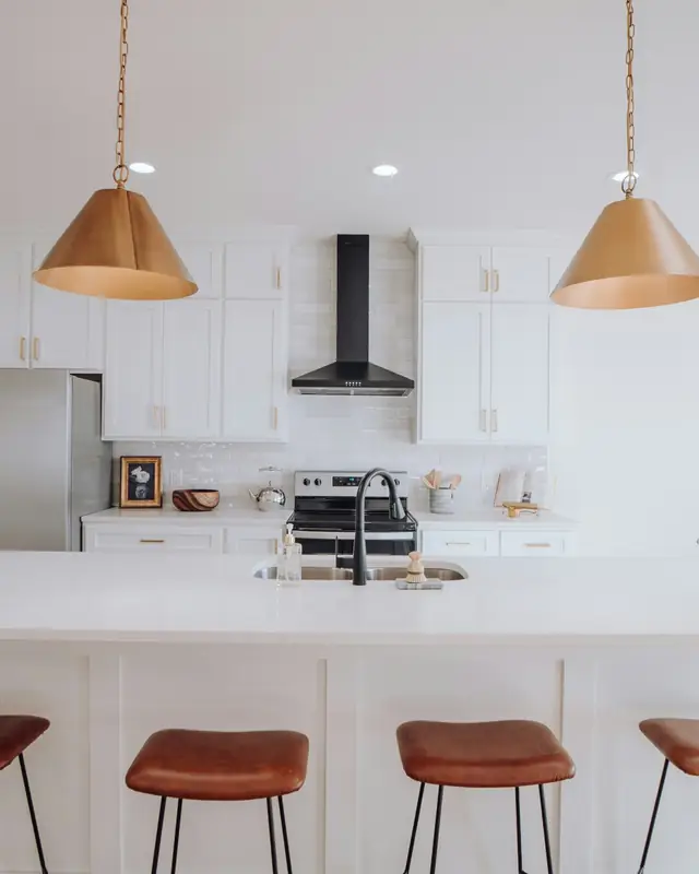 White kitchen with shaker cabinets, a large quartz island, leather stools and brass cone pendants
